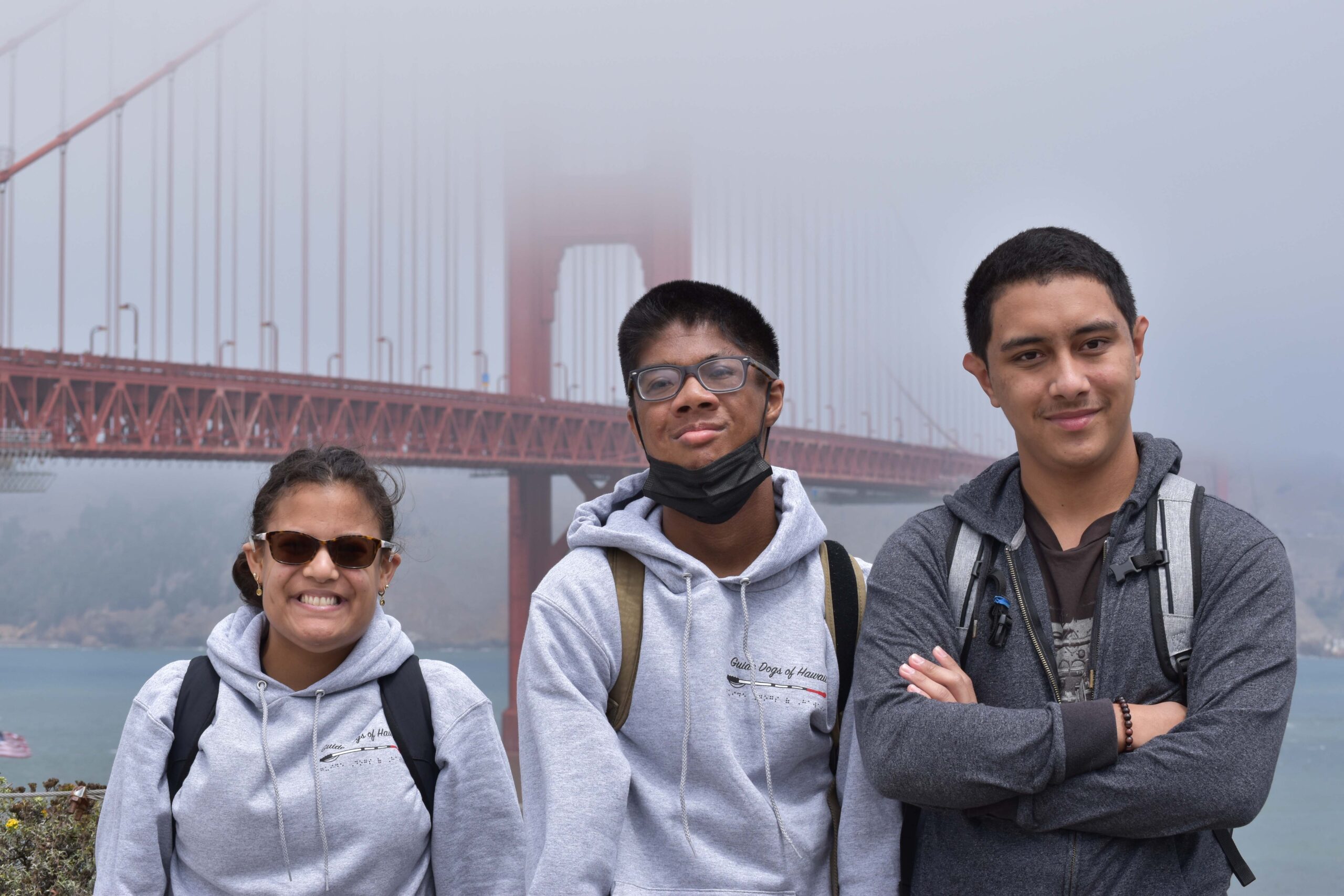 three people standing in front of the golden gate bridge.